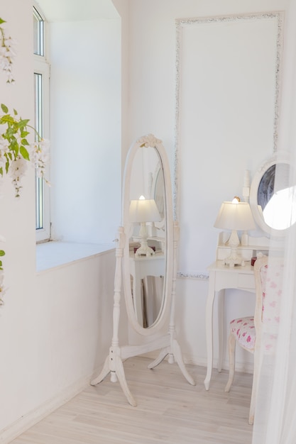 Tavolo da boudoir in stile vintage con specchio e fiori. Stanza bianca luminosa. Immagine verticale. Interni di design di lusso.