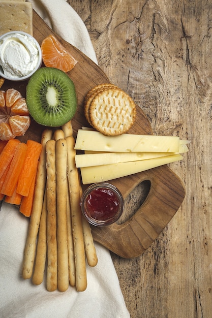 Tavolo da brunch sano da asporto con prosciutto, fragole; Kiwi; pane; biscotti; formaggio, carote, mandarini, hummus.