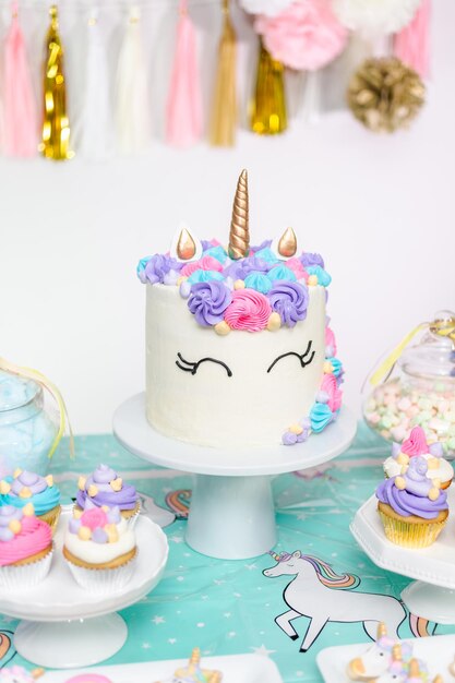 Tavolo da festa di compleanno per bambina con torta di unicorno, cupcakes e biscotti zuccherati.