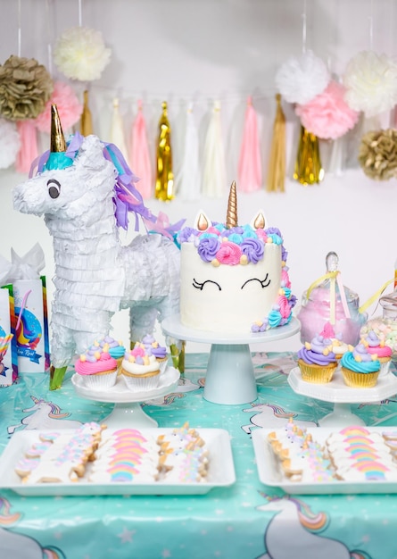 Tavolo da festa di compleanno per bambina con torta di unicorno, cupcakes e biscotti zuccherati.