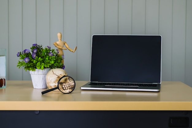 Tavolo da lavoro in legno decorato con vaso di fiori viola, teschio, vetro ingrandente e labtop