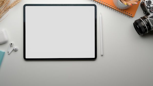 Tavolo da lavoro moderno con tablet schermo vuoto, tazza da tè, fotocamera, cancelleria e auricolare wireless
