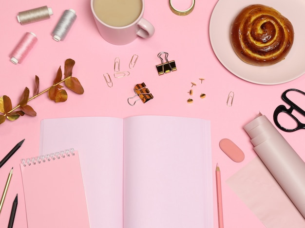Tavolo da lavoro rosa con carta per appunti, accessori per ufficio, caffè, forno