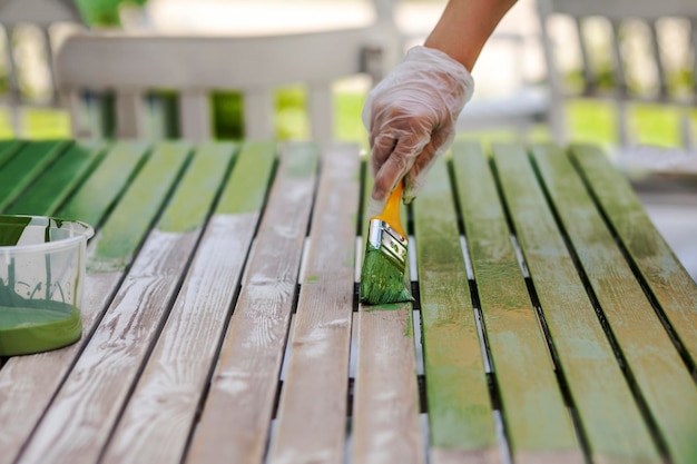 Tavolo da pittura con pennello. Il lavoratore dipinge il tavolo da giardino. Rinnovamento, Ristrutturazione Mobili da Giardino in Legno