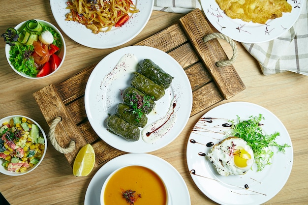 Tavolo da pranzo con molti piatti: dolama, insalata di verdure, zuppa, bistecca di manzo con uovo e dessert. Vista dall'alto, cibo piatto disteso