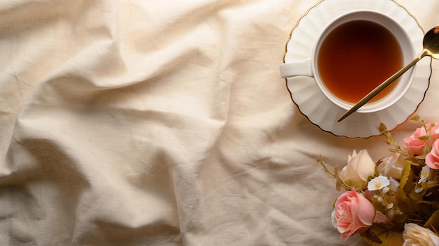 Tavolo da tè pomeridiano inglese con bella tazza da tè in ceramica, bouquet di rose e spazio per la copia su una tovaglia bianca minima. vista dall'alto