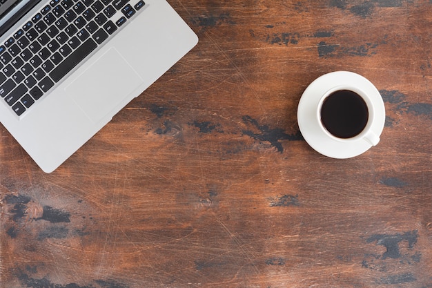 Tavolo da ufficio in legno scuro con computer portatile e tazza di caffè.