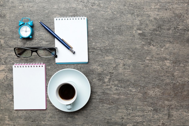 Tavolo da ufficio moderno con taccuino e altre forniture con tazza di caffè. Pagina del taccuino in bianco per la progettazione. Vista dall'alto, distesa.