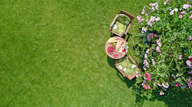 Tavolo decorato con pane, fragole e frutta nel bellissimo roseto estivo, vista dall'alto aerea della romantica data tabella cibo impostazione per due dall'alto