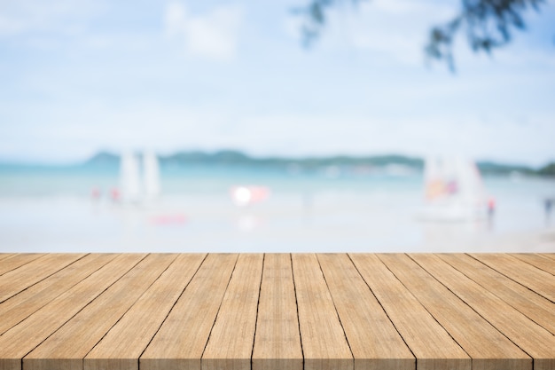 Tavolo di legno vuoto davanti con sfondo sfocato in spiaggia e barca a vela, spazio per montare i prodotti