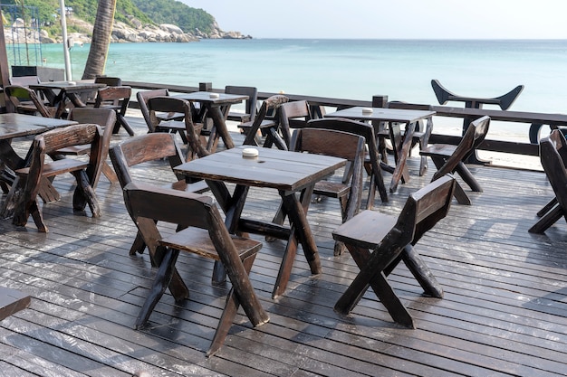 Tavolo e sedie in legno nel caffè vuoto sulla spiaggia vicino all'acqua di mare. Avvicinamento. Isola di Koh Phangan, Thailandia