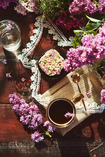 Tavolo estetico primaverile con cupcake floreale rosa fiori lilla tazza da caffè sotto ombre dure posate piatte