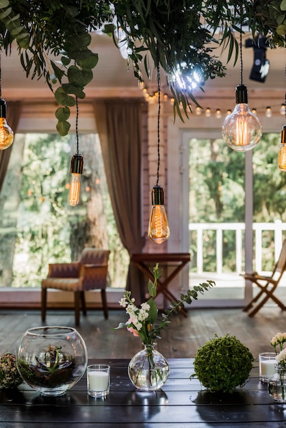 Tavolo festivo con bulbi di ghirlanda di Edison appesi ai lacci, decorati da rami di fiori verdi. effetto granuloso