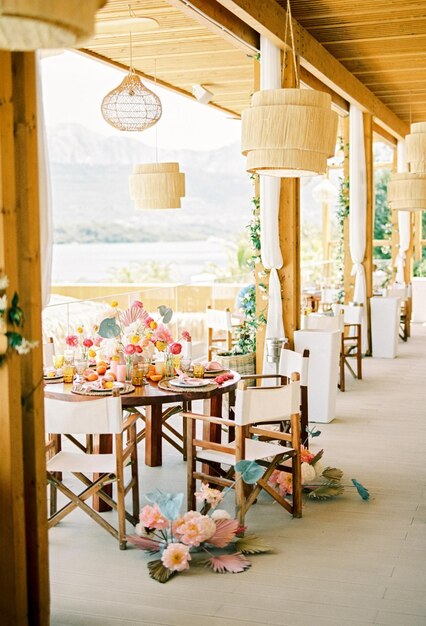 Tavolo festivo rotondo con bouquets di fiori sulla terrazza dell'hotel con lampadari di vimini e mare