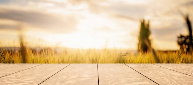 Tavolo in legno con sfondo sfocato di campo di grano e tramonto per la visualizzazione del prodotto