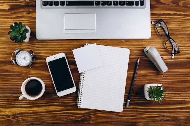 Tavolo in legno con una tazza di caffè, sveglia, computer portatile, smartphone, aereo, macchina fotografica