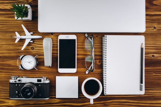 Tavolo in legno con una tazza di caffè, sveglia, computer portatile, smartphone, aereo, macchina fotografica