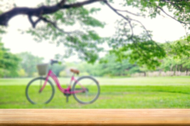 Tavolo in legno naturale astratto con bicicletta rosa sfocata su sfondo di erba verde