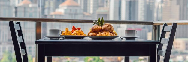 Tavolo per la colazione con caffè, frutta e pane croissant su un balcone sullo sfondo del grande