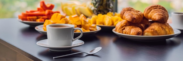 Tavolo per la colazione con caffè, frutta e pane croissant su un balcone sullo sfondo della grande città BANNER formato lungo