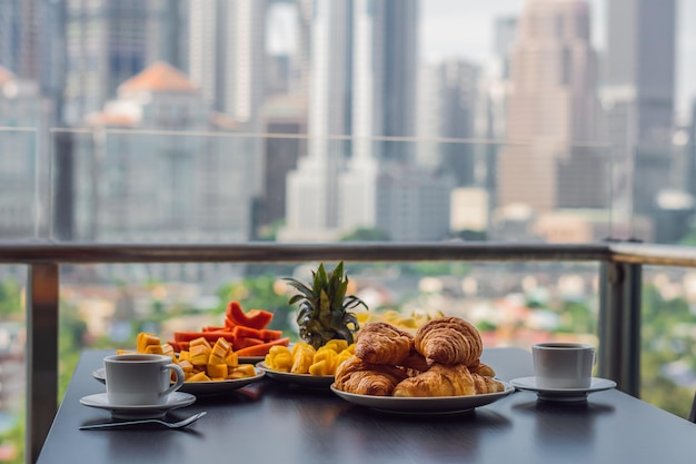 Tavolo per la colazione con frutta al caffè e croissant di pane su un balcone sullo sfondo del grande