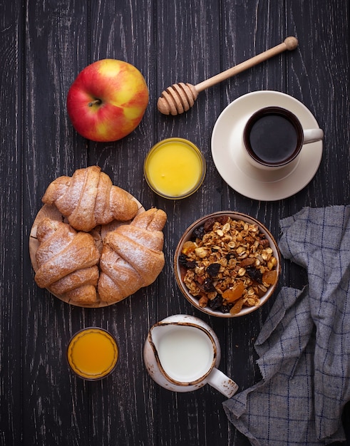 Tavolo per la colazione con muesli, croissant, mela, caffè, succo di frutta