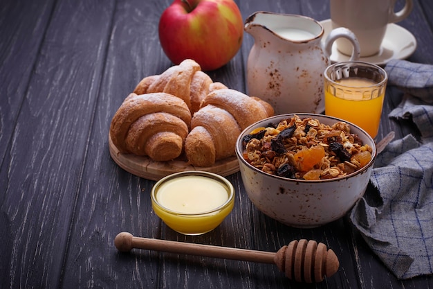 Tavolo per la colazione con muesli, croissant, mela, caffè, succo di frutta