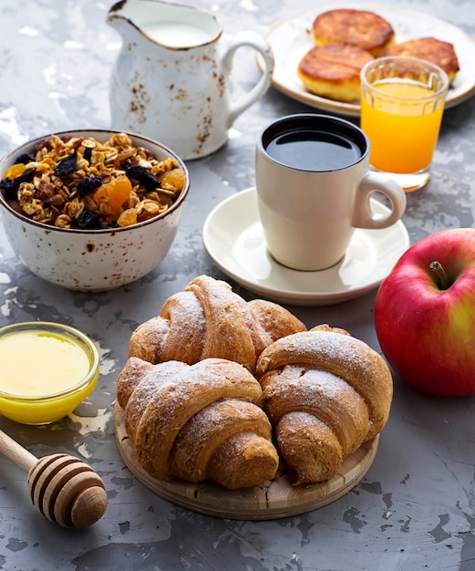 Tavolo per la colazione con muesli, croissant, mela, caffè, succo di frutta.