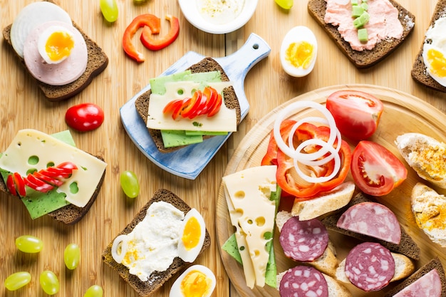 Tavolo per la colazione con panini al formaggio, salsiccia, verdure, uova sode e frutta