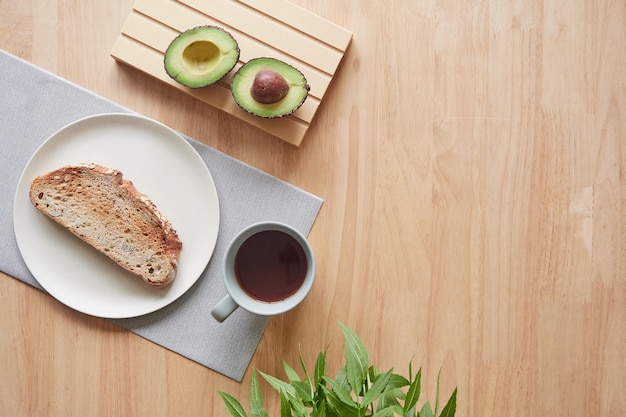 Tavolo per la colazione minimalista con una tazza di caffè tostato su un piatto e avocado tagliato a metà Concetto di alimentazione sana Vista dall'alto con spazio per la copia