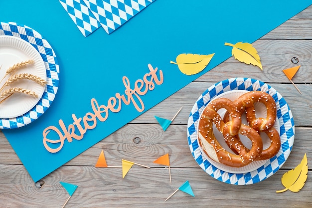 Tavolo rustico dell'Oktoberfest con prezel in piatti di carta, bandiere di carta e foglie di autunno.