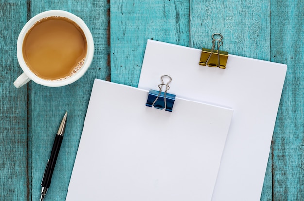 Tavolo scrivania in legno blu con risme di carta, penna e tazza di caffè.