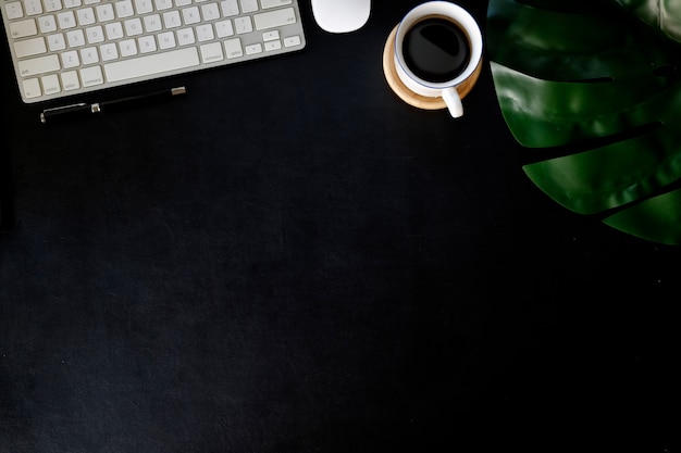 Tavolo scrivania in pelle ufficio con computer portatile, forniture, tazza di caffè e fiori.