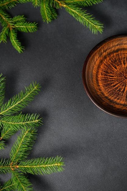 Tavolo scuro con rami di albero di Natale verdi sul tavolo a sinistra con un piatto vuoto sul lato destro