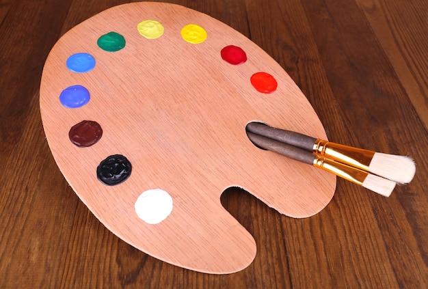 Tavolozza d'arte in legno con vernice e pennelli sul primo piano del tavolo