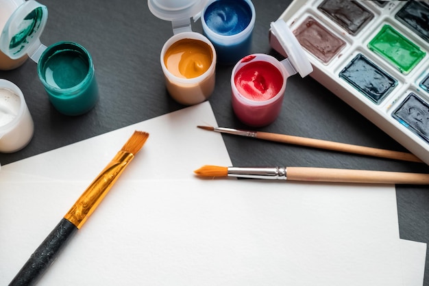 Tavolozza di lattine di vernici ad acquerello con pennelli a pigmenti colorati e carta sul tavolo pronta per il disegno