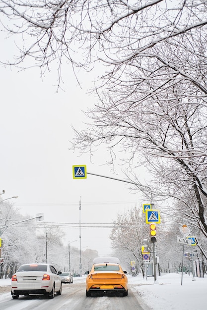 Taxi giallo e auto bianca al semaforo in una giornata nevosa invernale La neve sulla strada degli alberi viene spazzata