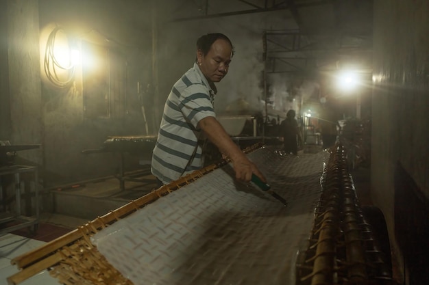 Tay Ninh VIETNAM JULIO 07 2023 Focus uomo del villaggio tradizionale che preparava cibo alla noodle stavano asciugando la noodle fresca su una griglia di legno per il mercato concetto di stile di vita