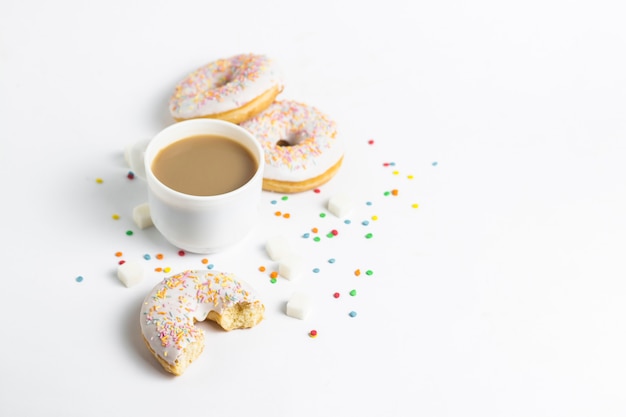 Tazza bianca, caffè o tè al latte e gustose ciambelle fresche, dolci caramelle decorative multicolori su uno sfondo bianco. Concetto di panetteria, pasticceria fresca, deliziosa colazione, fast food.