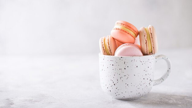 Tazza bianca con amaretti colorati su bianco, copia dello spazio