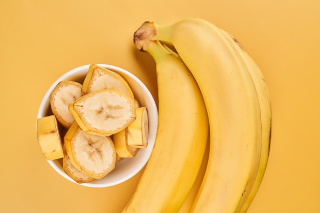 Tazza bianca con banane a fette su sfondo giallo. Frutti tropicali, cibo sano, vitamine