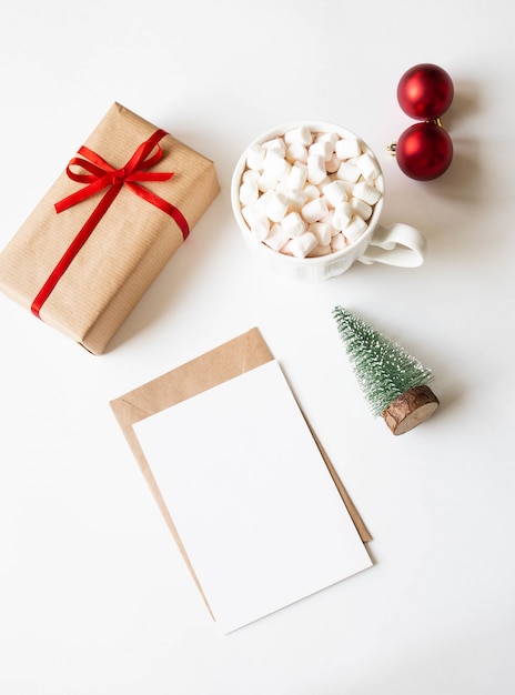 Tazza bianca con bevanda calda e marshmallow, carta di carta per lettera, busta e decorazioni natalizie