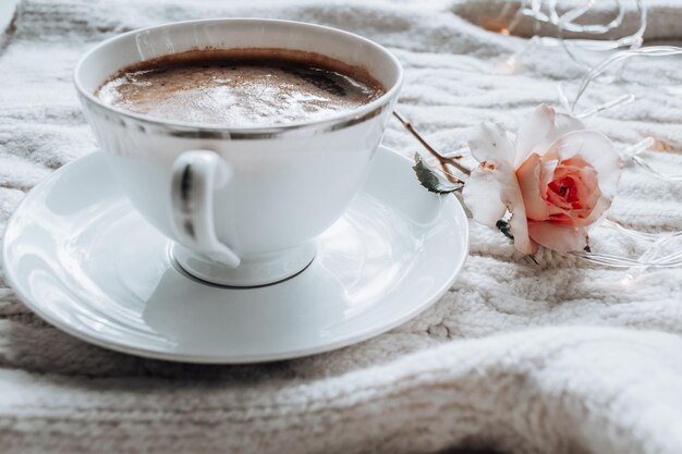 Tazza bianca con caffè nero e rosa tea su un plaid lavorato a maglia bianco