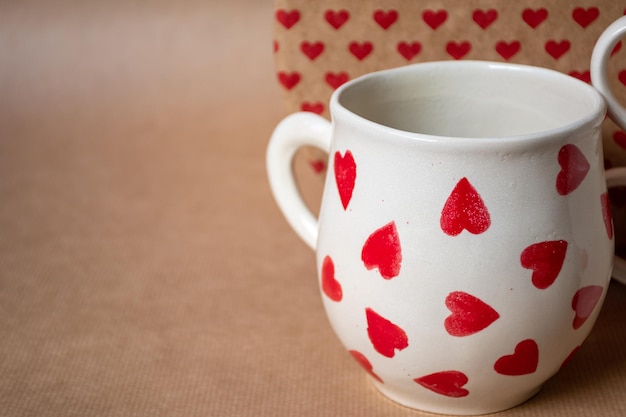 Tazza bianca con molti cuori rossi e sfondo di carta artigianale