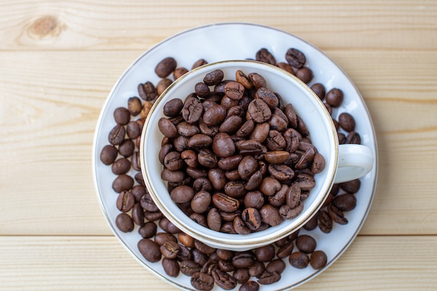 Tazza bianca con tazza di caffè in grani su sfondo di legno con messa a fuoco selettiva e frammento di raccolto.