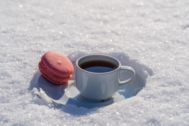 Tazza bianca di caffè caldo con amaretto rosa su un letto di neve e sfondo bianco da vicino