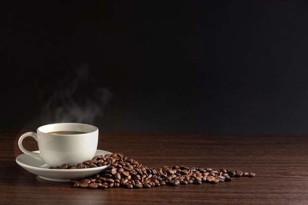 Tazza bianca di caffè caldo con fumo con i chicchi di caffè e su fondo nero