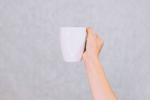 Tazza bianca per caffè, tè nella mano della ragazza. Su uno sfondo bianco.