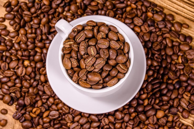 Tazza bianca piena di chicchi di caffè su tavola di legno rustica. Vista dall'alto