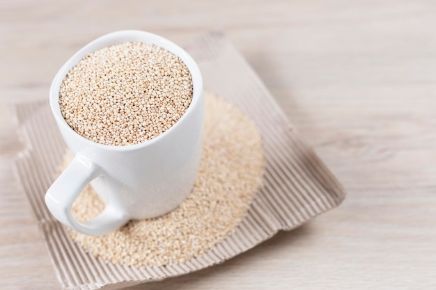 Tazza bianca piena di chicchi di quinoa su fondo di legno